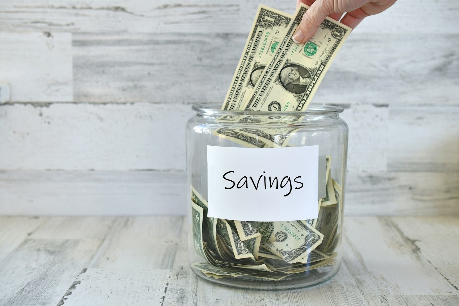 Jar of money cash with hand inserting dollar bills for savings of funds